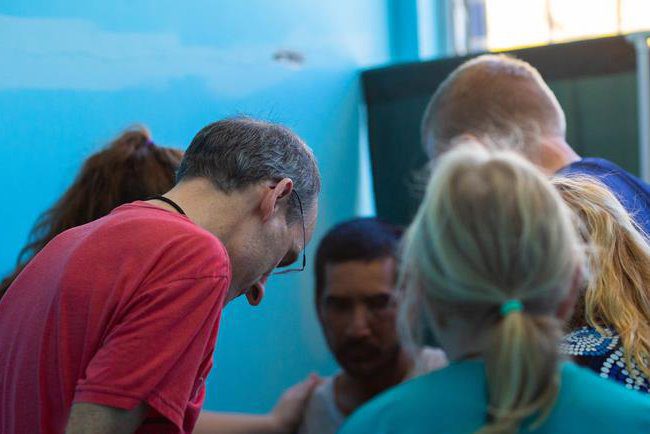 A man in a red shirt and five volunteers standing around him with their eyes closed.