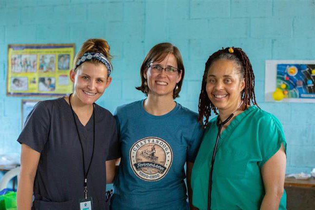 Three female volunteers standing together smiling in a medical clinic.