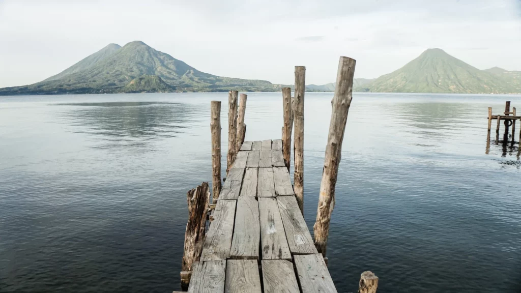 A wooden dock leading into the water with mountains in the background.