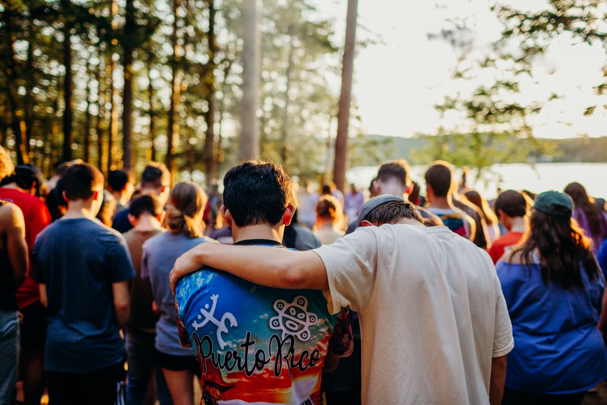 A crowd of students at an outdoor youth camp with their heads bowed in prayer.