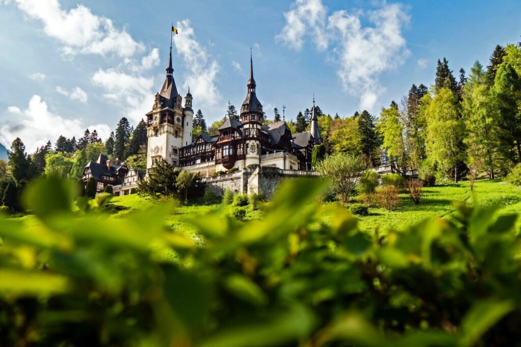 Beautiful castle with the Romanian flag set against a sunny blue sky. Photo by Majkl Velner on Unsplash.